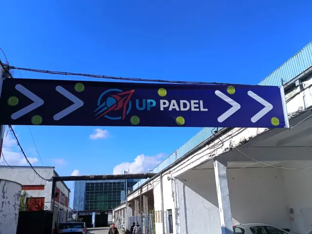 Banner UP PADEL montat deasupra unei alei, cu săgeți albe și mingi verzi.
