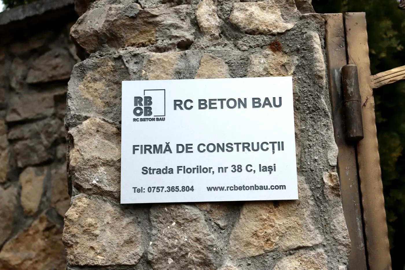 Placă RC Beton Bau pentru firmă de construcții, fixată pe un stâlp din piatră.