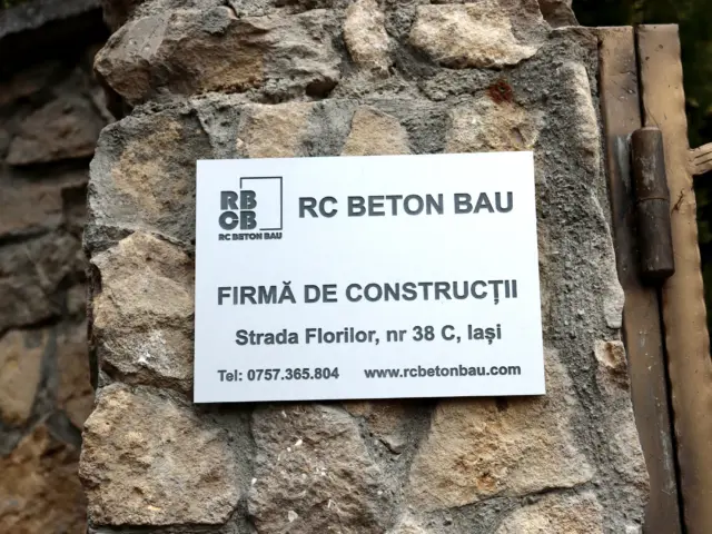 Placă de identificare RC Beton Bau, montată pe un stâlp din piatră, cu adresă și date de contact.