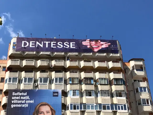 Mesh Dentesse montat deasupra balcoanelor unei clădiri, cu portret și mesaj de brand.
