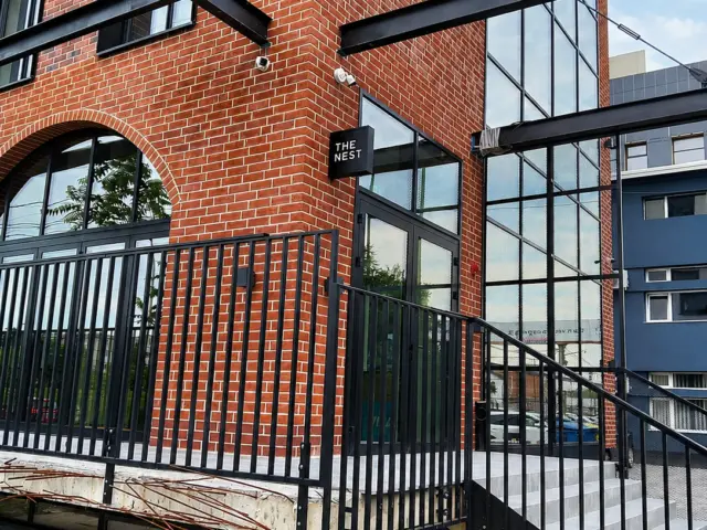 The Nest projecting sign mounted beside the entrance of a brick-clad building.