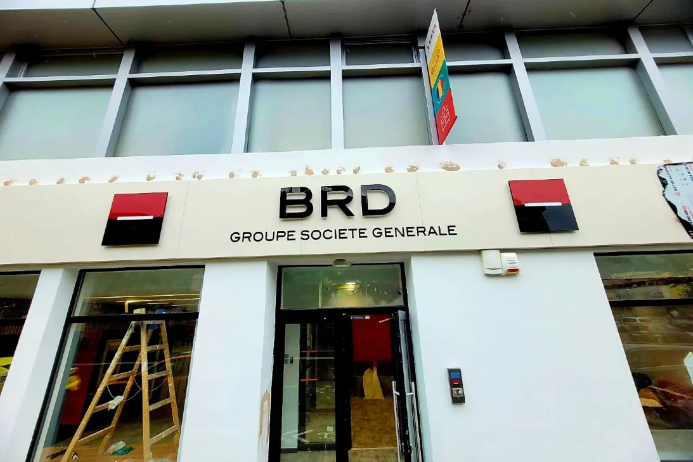 Litere volumetrice BRD și două embleme montate deasupra intrării, cu o scară vizibilă în interior.