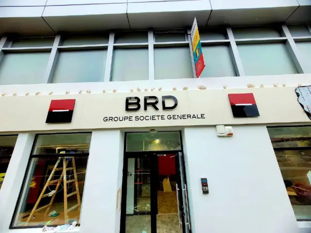 Litere volumetrice BRD și două embleme montate deasupra intrării, cu o scară vizibilă în interior.