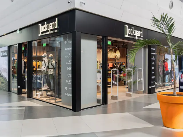 Două inscripții luminoase Dockyard Stores montate pe fațada neagră a unui magazin din centrul comercial.