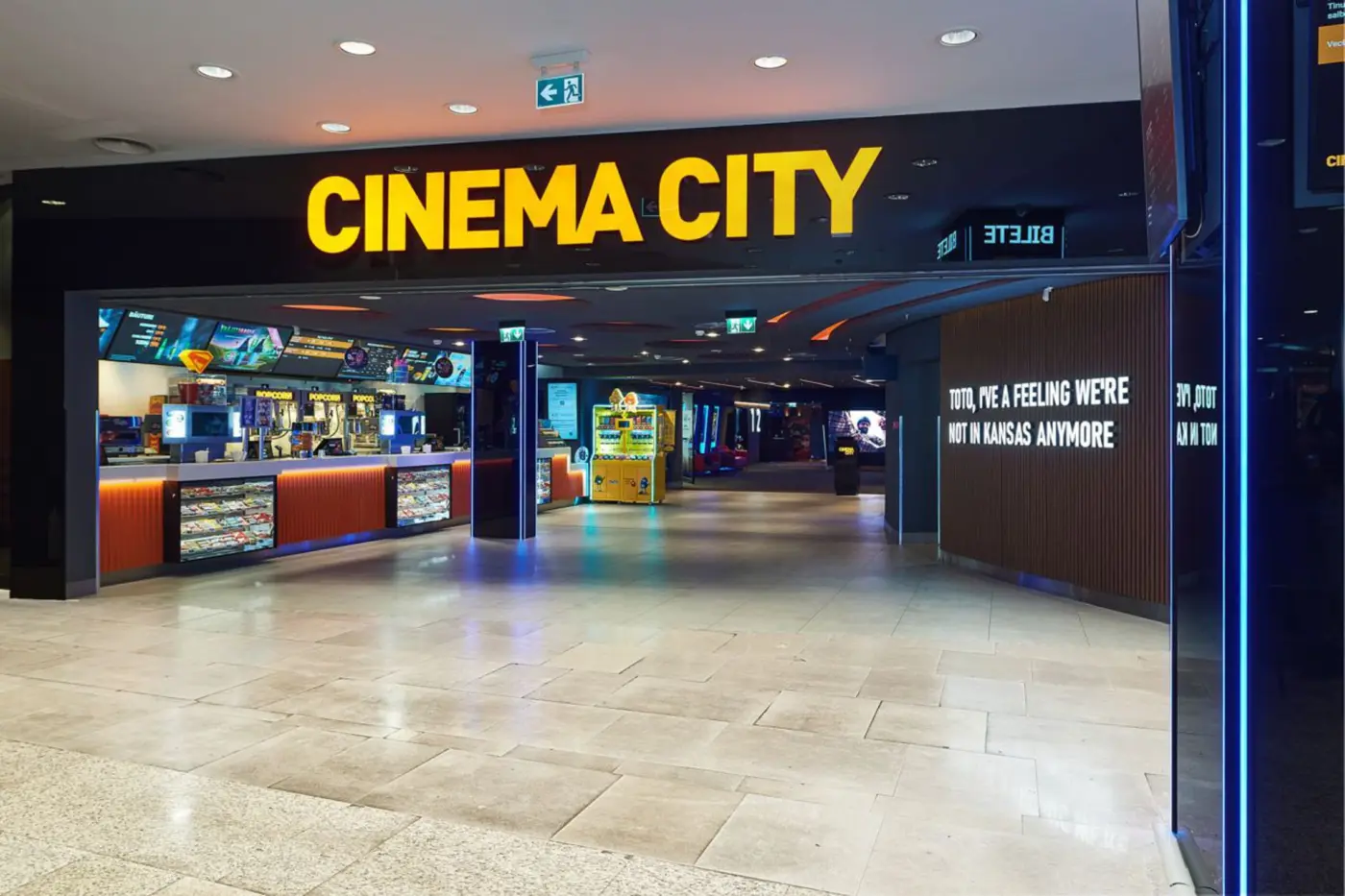Litere volumetrice galbene CINEMA CITY deasupra accesului, cu zona de concesiuni vizibilă în interior.