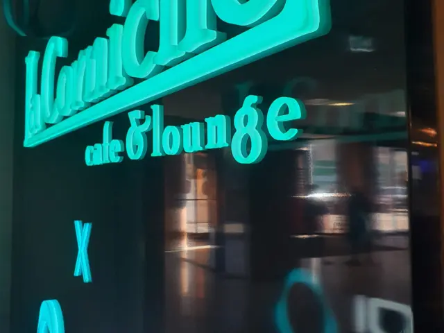 Litere volumetrice turcoaz aprinse, cu textul „cafe & lounge”, montate pe o suprafață neagră lucioasă.