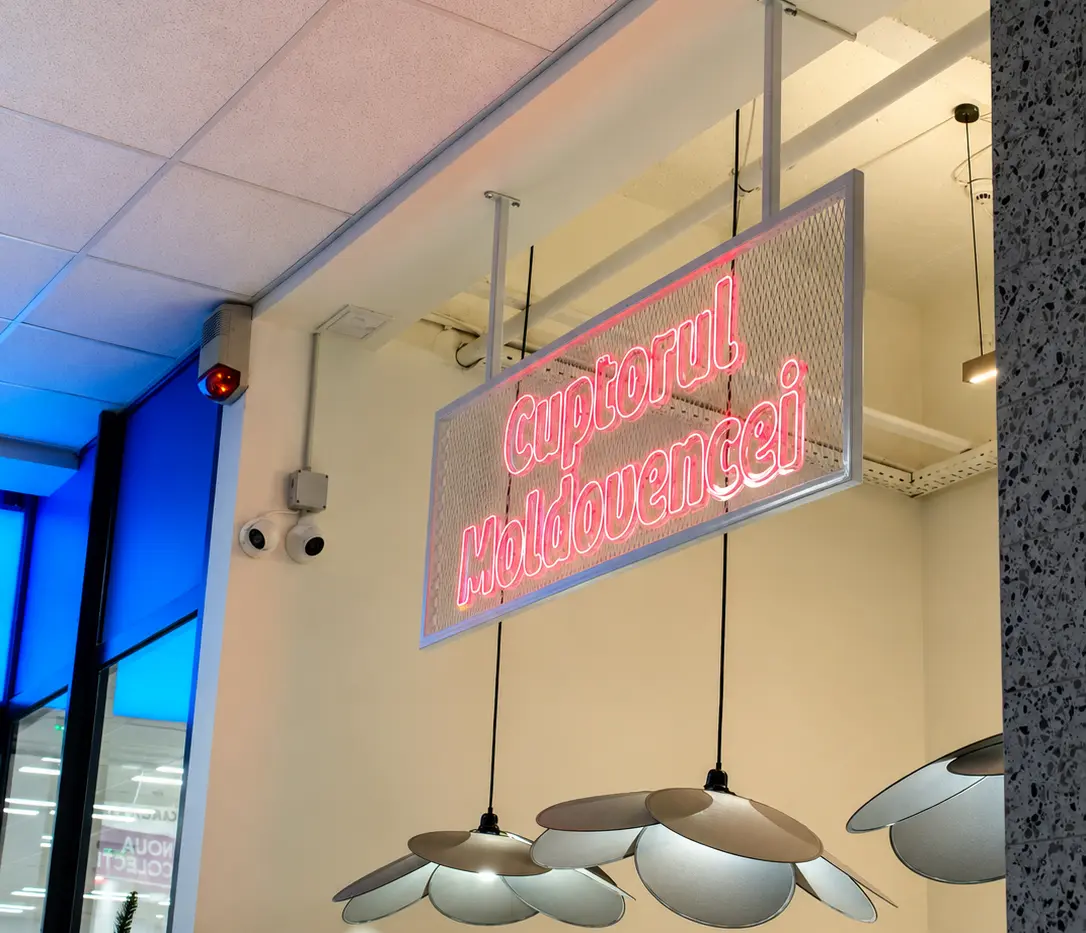Semn Neon Flex roz „Cuptorul Moldovencei”, suspendat pe un panou tip plasă într-un spațiu interior.