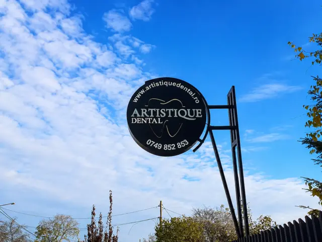 Round Artistique Dental sign mounted on a black metal frame against a blue sky