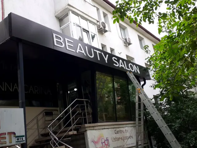 Litere volumetrice albe „BEAUTY SALON” pe o copertină neagră, cu o scară sprijinită de fațadă.