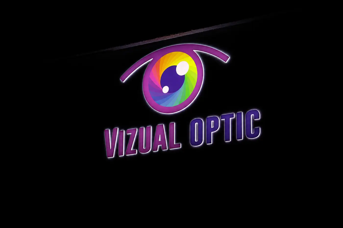Firmă luminoasă Vizual Optic, cu litere volumetrice și simbol multicolor în formă de ochi, prezentată pe fundal întunecat.