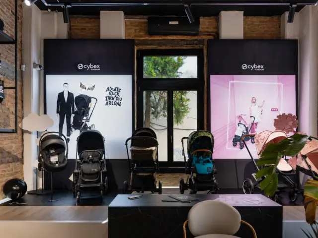 Două reclame luminoase Cybex Platinum, amplasate în showroom în spatele mai multor cărucioare pentru copii.