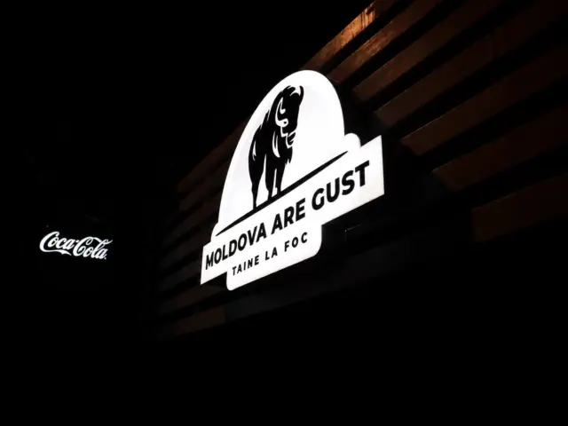 Illuminated Moldova Are Gust sign with a stylized bison, mounted on a dark slatted facade.