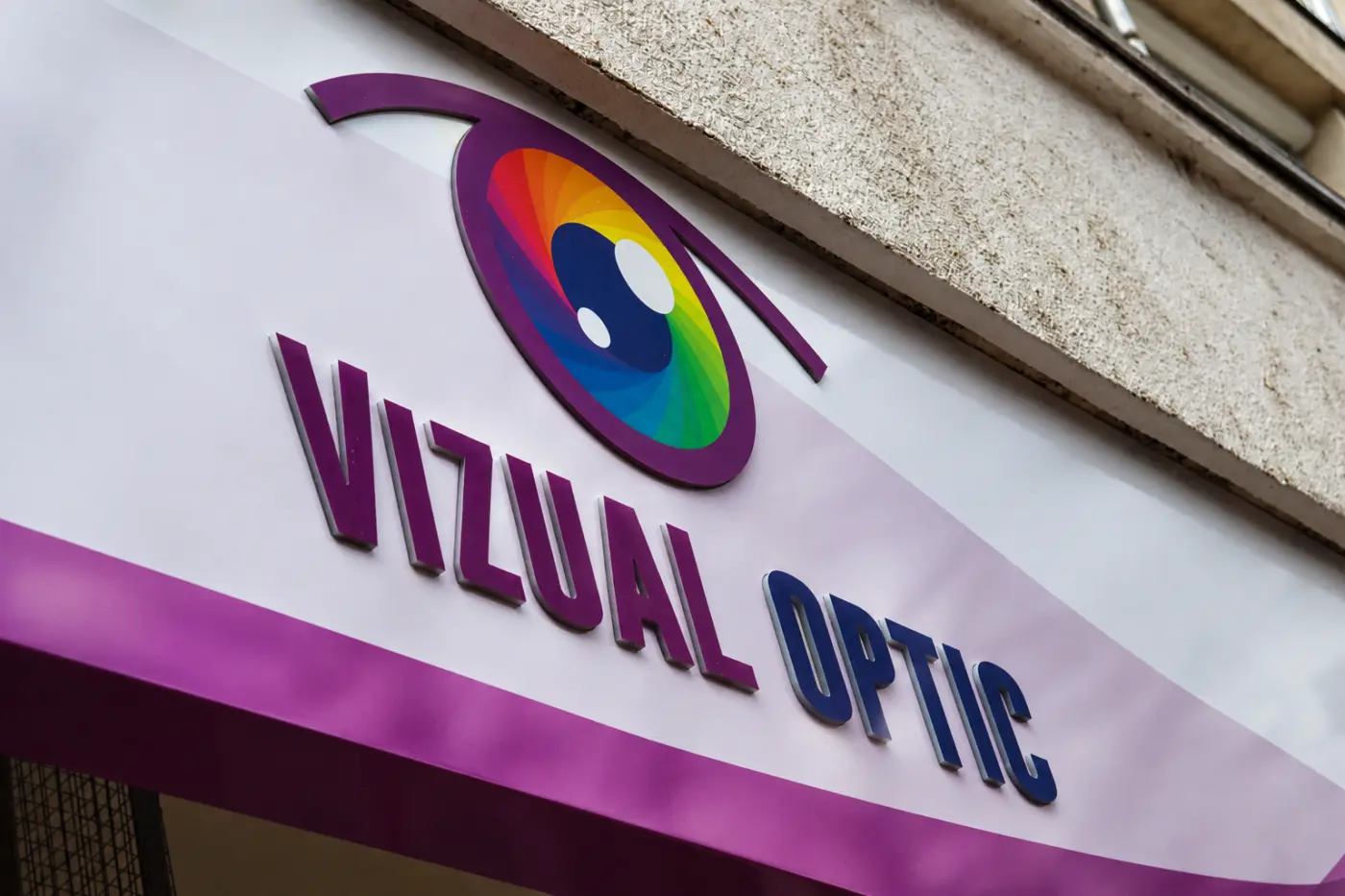 Sigla multicoloră și literele volumetrice Vizual Optic, montate pe un panou alb de fațadă.