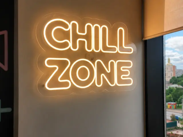 Semn luminos „Chill Zone”, montat pe suport transparent lângă o fereastră.