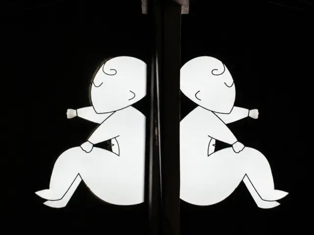 White illuminated sign featuring two stylized figures arranged symmetrically around a central vertical element at night.