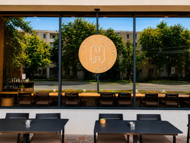 Circular Horn Artisan Spirit sign mounted on a window above outdoor dining tables.