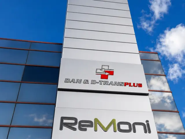 Siglele volumetrice Dan & D-Transplus și ReMoni, montate pe coloana albă a unei fațade vitrate.