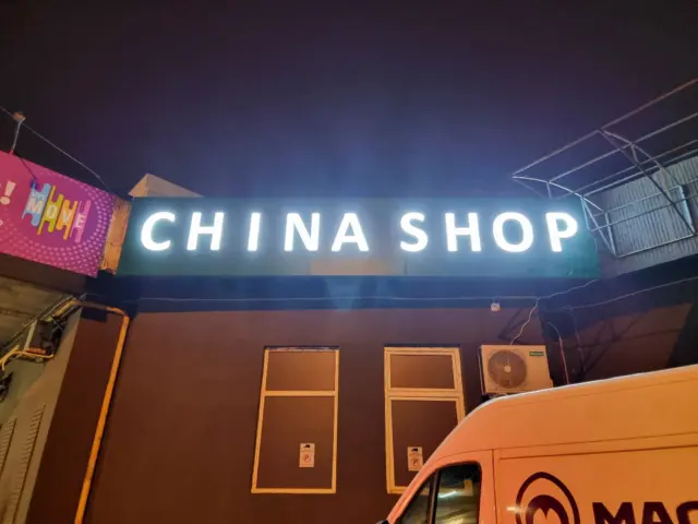 Literele luminoase CHINA SHOP sunt montate în partea superioară a unei fațade întunecate, văzută noaptea.