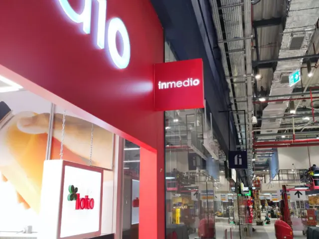 Firmă roșie inmedio, montată perpendicular deasupra vitrinei, într-un spațiu comercial interior.