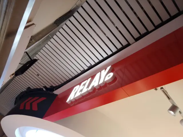 Litere volumetrice luminoase RELAX, montate pe o bandă roșie într-un spațiu comercial interior.