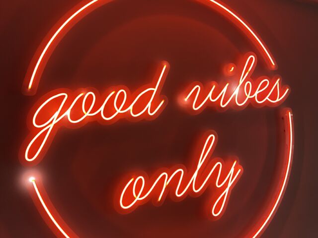 Inscripția cursivă „good vibes only”, luminată în roșu și încadrată circular, montată pe un perete interior.
