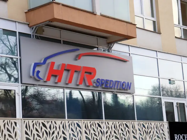 Logo HTR Spedition cu litere volumetrice roșii și albastre, montat pe un panou deasupra intrării.