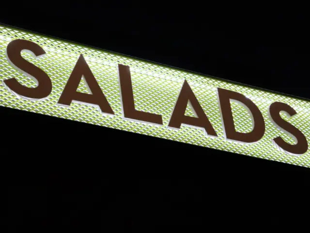 Inscripția SALADS cu litere volumetrice, montată pe un panou luminos cu model geometric, pe timp de noapte.