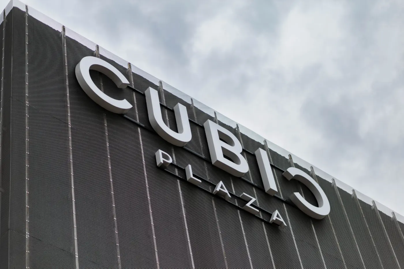 Firma CUBIC PLAZA cu litere volumetrice albe, montată pe o fațadă închisă la culoare.