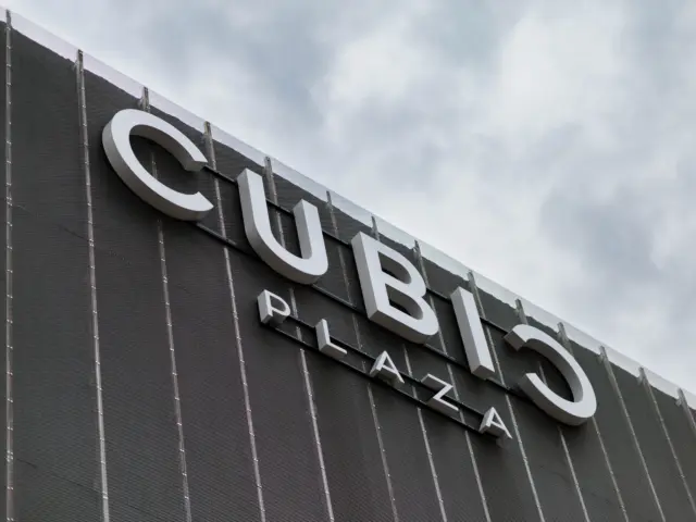 Firma CUBIC PLAZA cu litere volumetrice albe, montată pe o fațadă închisă la culoare.