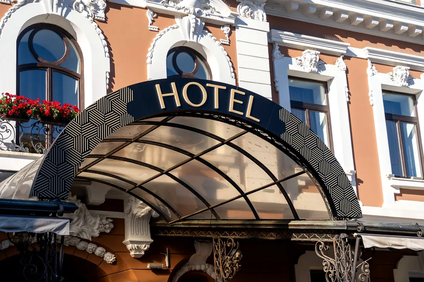 Litere volumetrice aurii „HOTEL”, montate pe o copertină arcuită, în fața unei clădiri cu fațadă ornamentată.