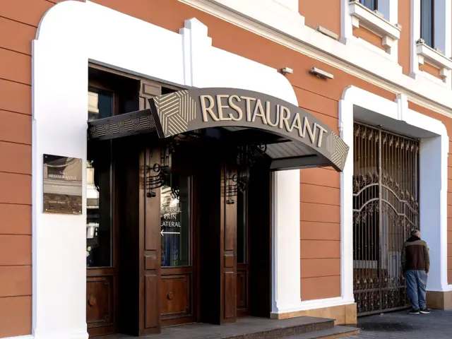 Litere volumetrice aurii RESTAURANT, montate pe copertina arcuită deasupra unei intrări stradale.