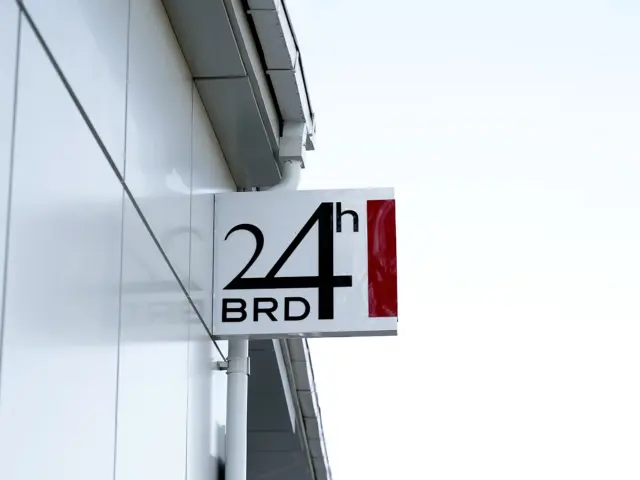 Rectangular BRD 24h sign mounted perpendicular to the facade of a modern building.