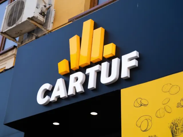 Logo-ul CARTUF cu litere volumetrice albe și elemente galbene, montat deasupra intrării.