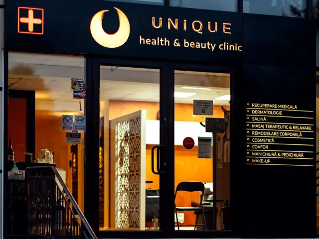 Firmă luminoasă Unique Health & Beauty Clinic, montată deasupra intrării vitrate, lângă lista de servicii.