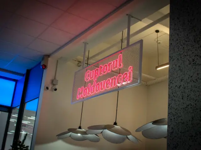 Inscripția roz „Cuptorul Moldovencei” din Neon Flex, montată pe un panou suspendat din plasă.