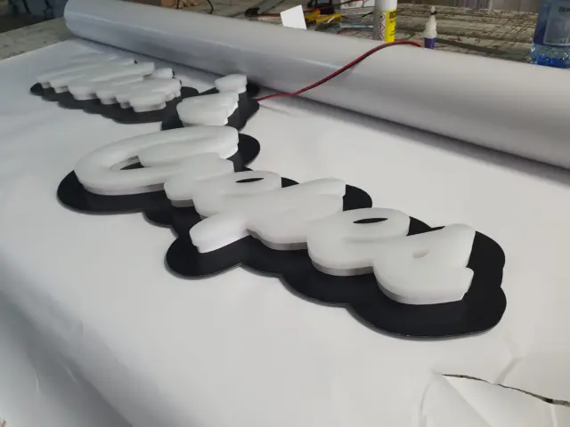 Ansamblu de litere volumetrice albe pe suporturi negre conturate, aflat în lucru pe masa din atelier.