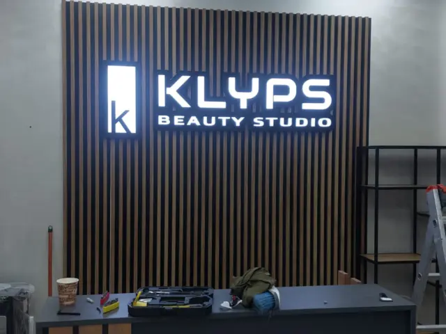 Sigla și literele luminoase KLYPS Beauty Studio, montate pe peretele cu lamele din zona recepției.