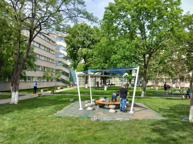 Structură metalică albă cu copertină albastră, în curs de montaj într-o curte verde.