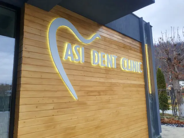 Logo în formă de dinte și litere luminoase ASI DENT CLINIC, montate pe fațada placată cu lemn.