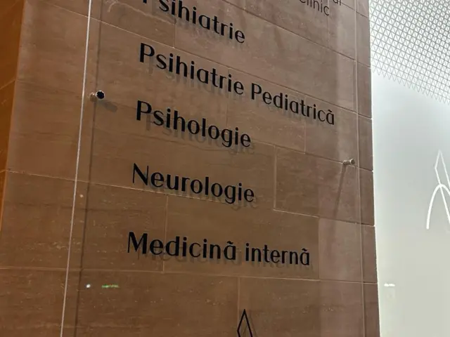 Placă transparentă ANOVA Medical Clinic, montată pe perete, cu lista specialităților medicale disponibile.