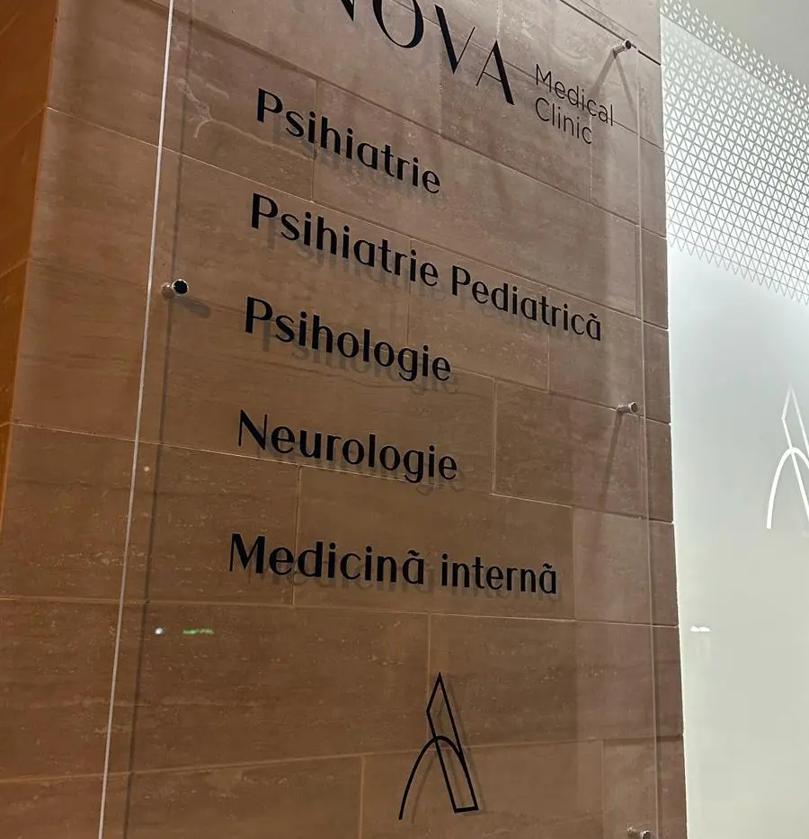 Placă transparentă ANOVA Medical Clinic, montată pe perete, cu lista specialităților medicale disponibile.