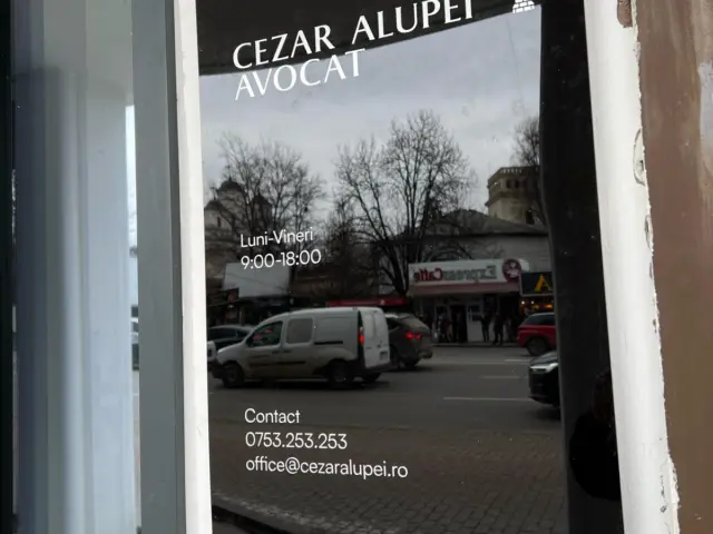 Placă informativă neagră Cezar Alupei Avocat, montată pe perete lângă o ușă vitrată.