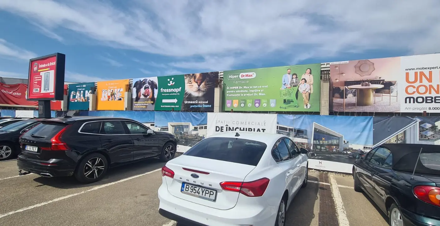 Ansamblu de bannere publicitare amplasate pe fațada unui centru comercial, deasupra parcării.