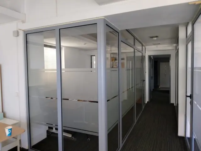 Autocolant mat aplicat pe compartimentări interioare din sticlă, cu benzi transparente orizontale.