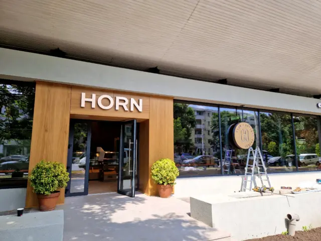 Litere volumetrice HORN deasupra intrării și emblemă circulară pe vitrină, cu scară și unelte alături.