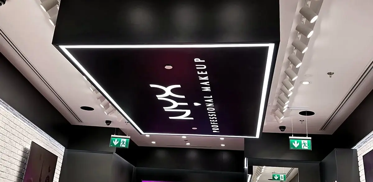 Panou luminos NYX Professional Makeup, montat pe plafon într-un spațiu comercial cu interior alb-negru.