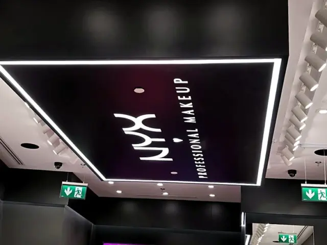 NYX Professional Makeup illuminated ceiling sign inside a black-and-white retail space.