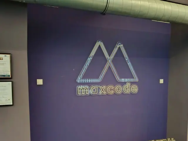 Sigla Maxcode din Neon Flex, montată pe un perete mov într-un spațiu interior.
