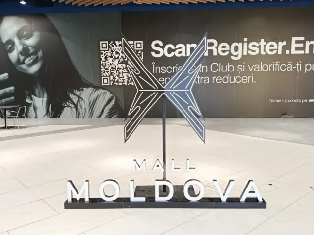 Instalație Mall Moldova cu emblemă geometrică luminoasă și litere albe, amplasată în interiorul centrului comercial.