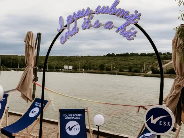 Mesaj violet din Neon Flex, montat pe un arc negru într-o zonă de relaxare lângă apă.